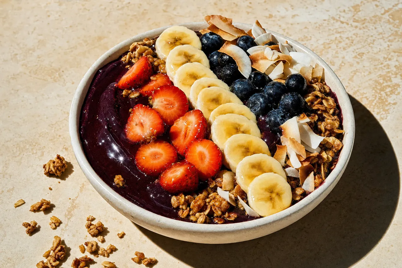 Açaí bowl blended thick and topped with banana coins, strawberries, blueberries, granola and toasted coconut on a limestone counter