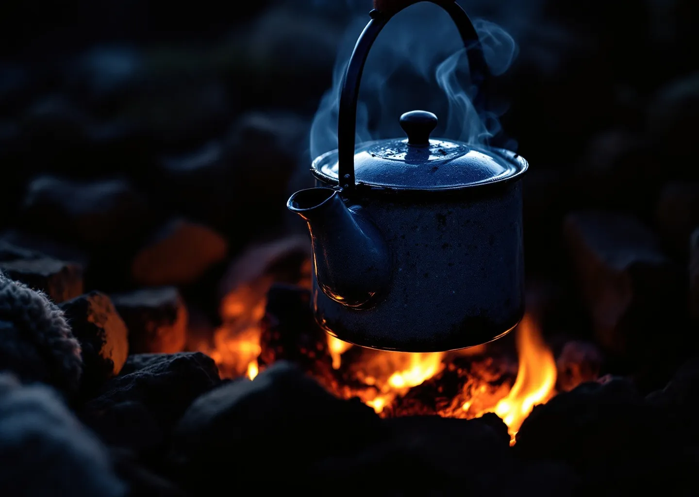 Blackened enamel kettle steaming over campfire coals at night