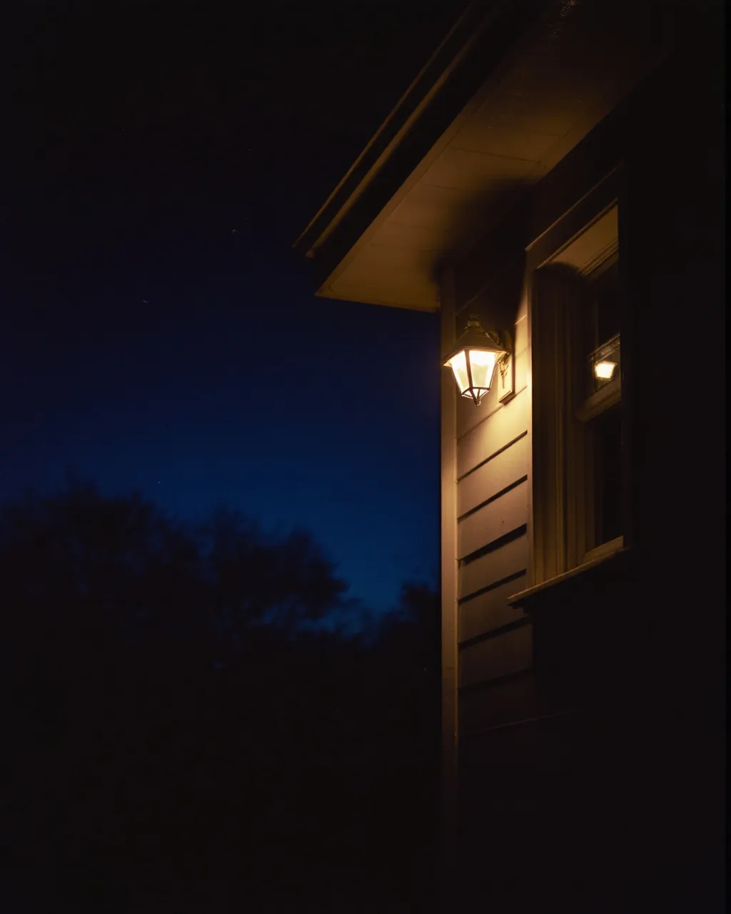 A single warm porch light on a dark house at night