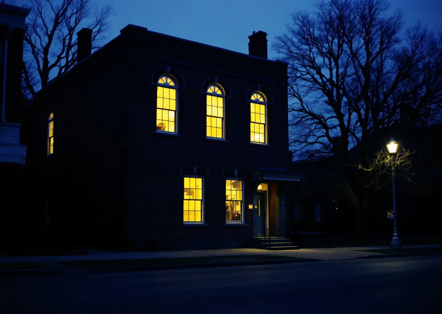The 1913 brick library at dusk, every window lit warm