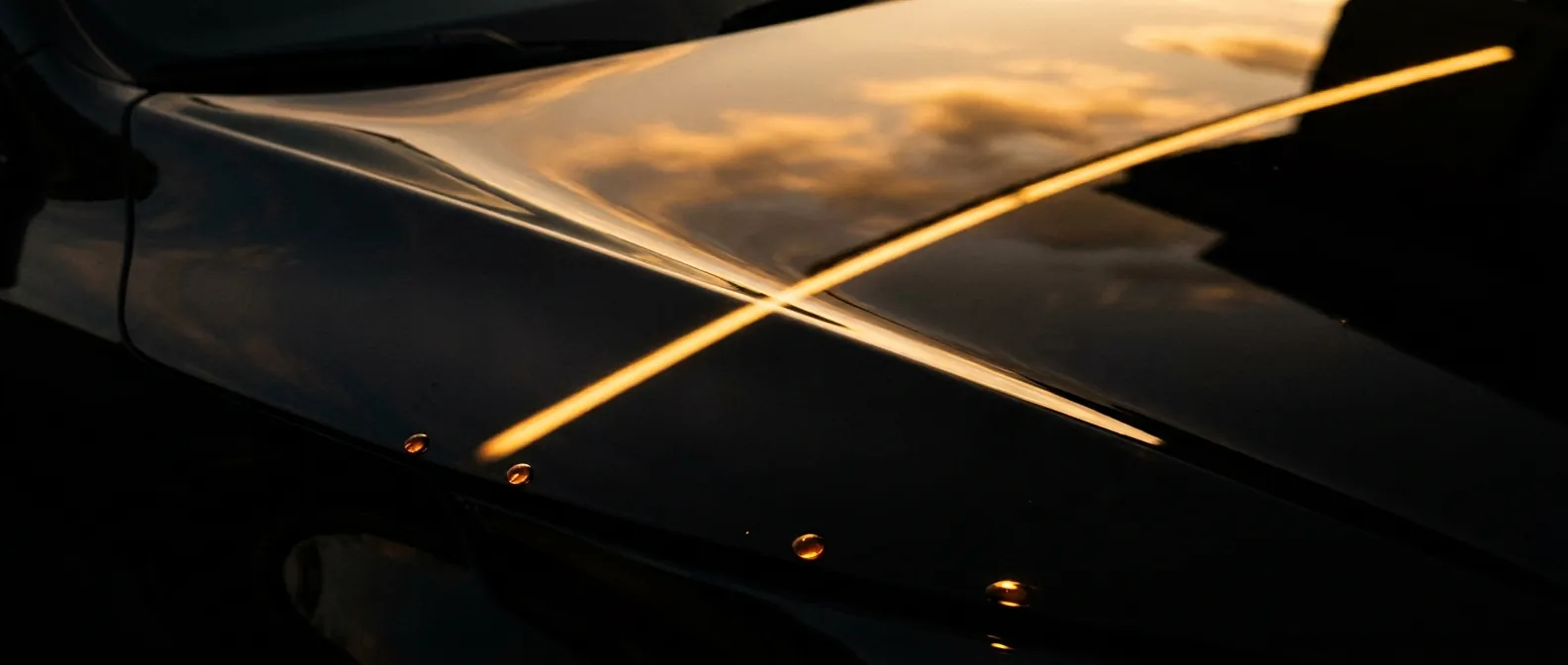 Freshly detailed black hood mirroring a golden-hour sky