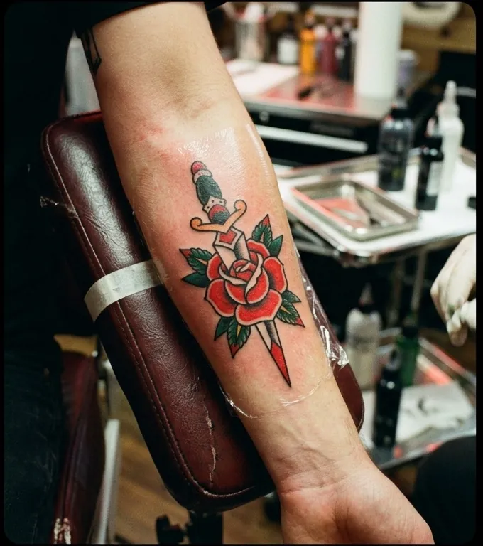Fresh dagger and rose tattoo on a forearm, wrapped edge visible, day zero