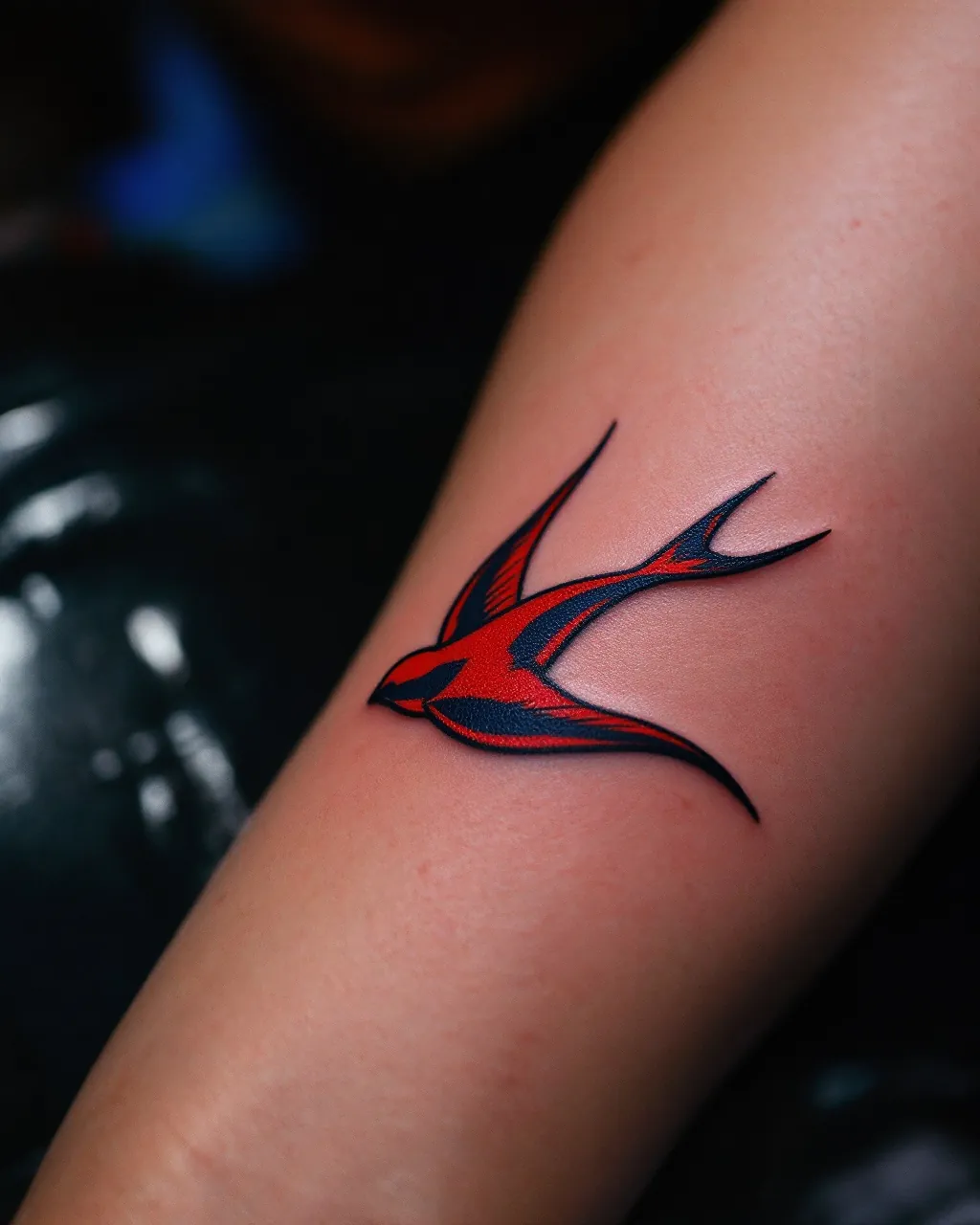 Red and black swallow tattoo on a forearm resting on the chair